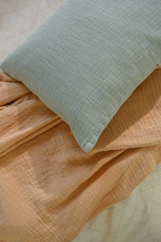 detail shot van een sprei in een oranje kleur en een sierkussensloop in een blauwe kleur