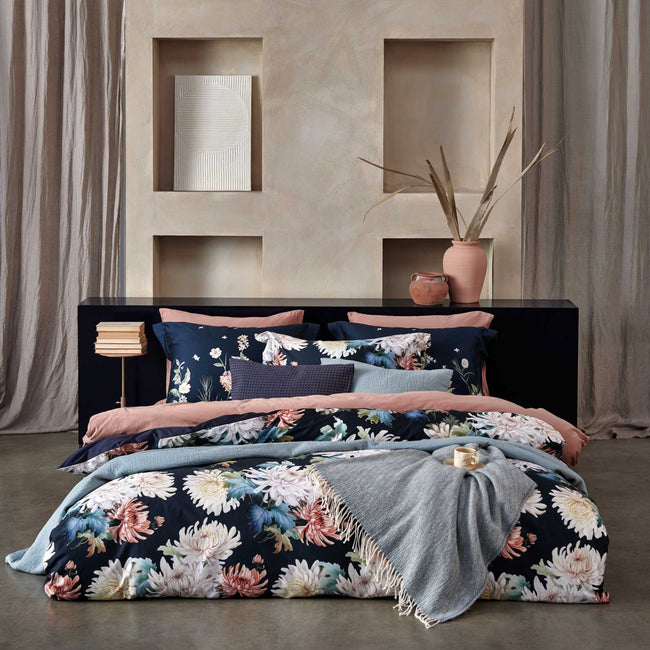 een bed in een rustige, serene omgeving met een bed met een dekbedovertrek in donkerblauw met daarop bloemen geprint, een dekbedovertrek in een roze kleur en een sprei van wol en katoen in een blauwe kleur