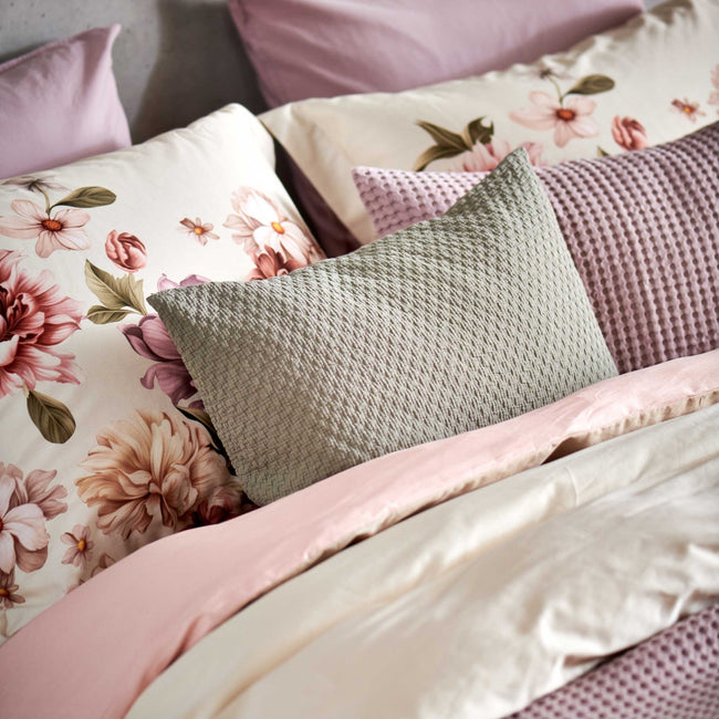 detail shot van een bed met een beige dekbedovertrek met roze en beige bloemen en sierkussens in lila en groene kleuren