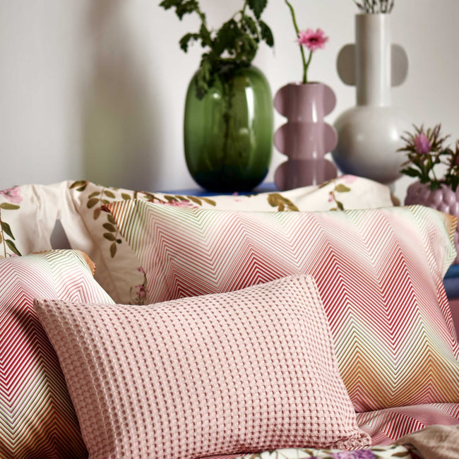 detail shot van een hoofdkussen met zigzag print in roze en oranje kleuren en een wafel sierkussen in roze